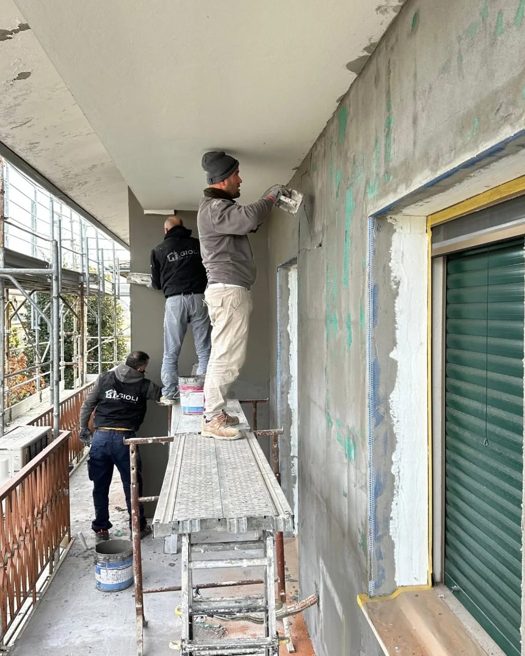 Operai GIOLI SRL con abbigliamento aziendale al lavoro su un ponteggio durante la rasatura di una facciata