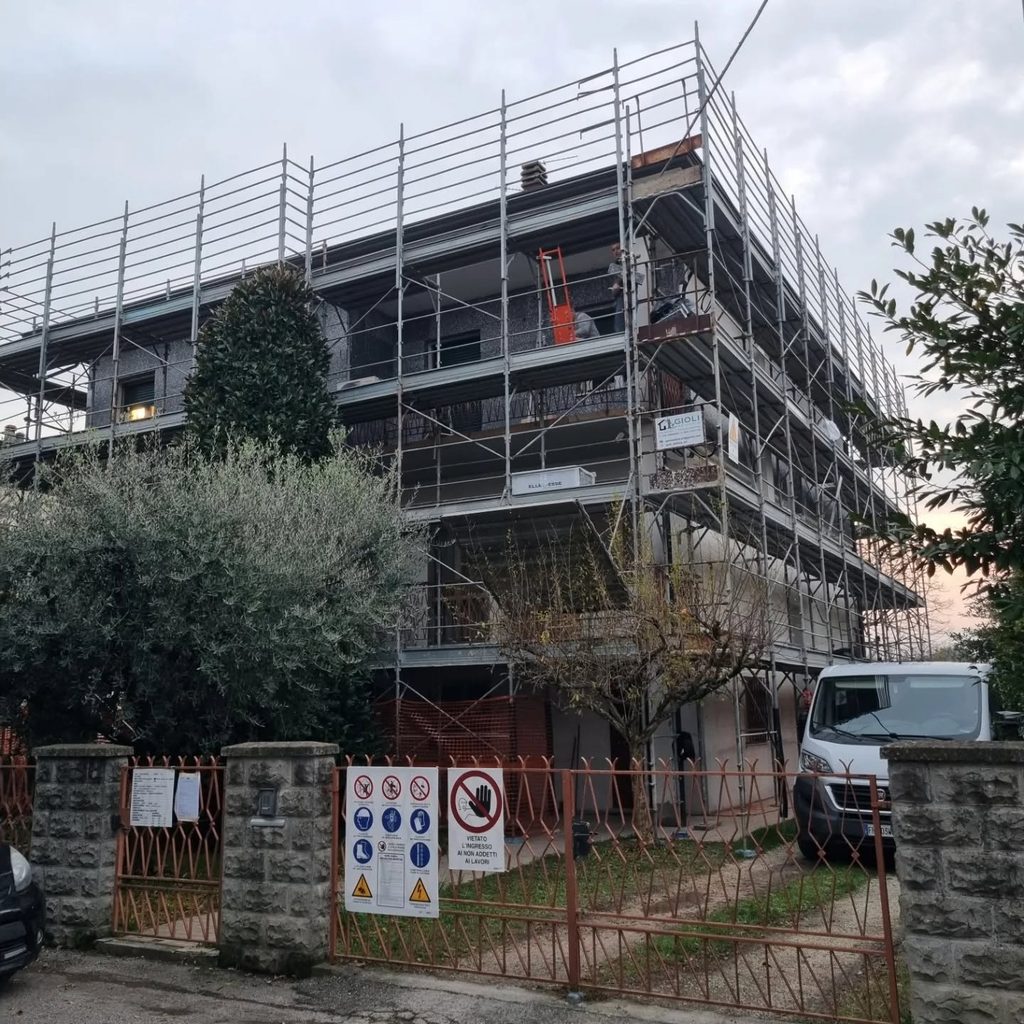 Edificio residenziale interamente ponteggiato durante la ristrutturazione, con cartellonistica di sicurezza e furgone aziendale