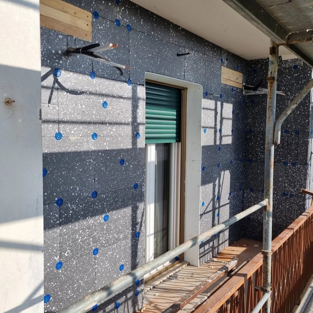 Posa di pannelli isolanti in EPS con grafite e tasselli di fissaggio attorno a una finestra con persiana verde