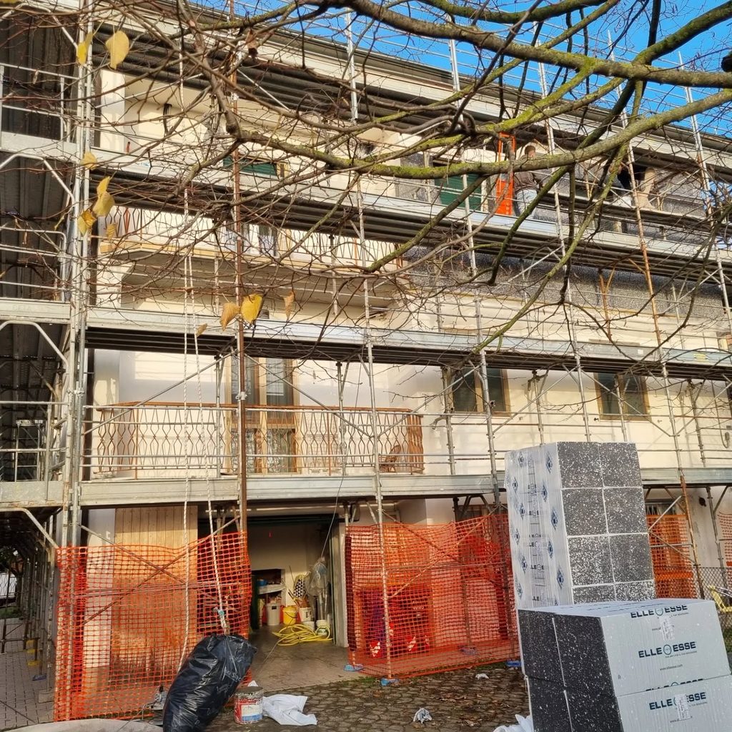 Condominio con ponteggio completo, reti di protezione arancioni e pacchi di pannelli isolanti in cantiere